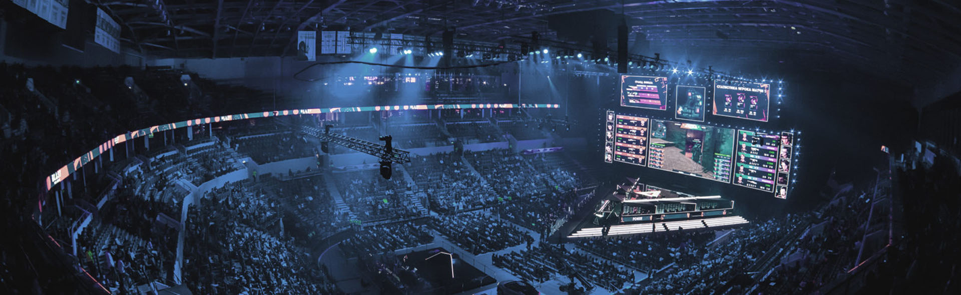 In einer Gaming-Arena folgen Menschen dem E-Sports-Wettkampf auf großen Bildschirmen.